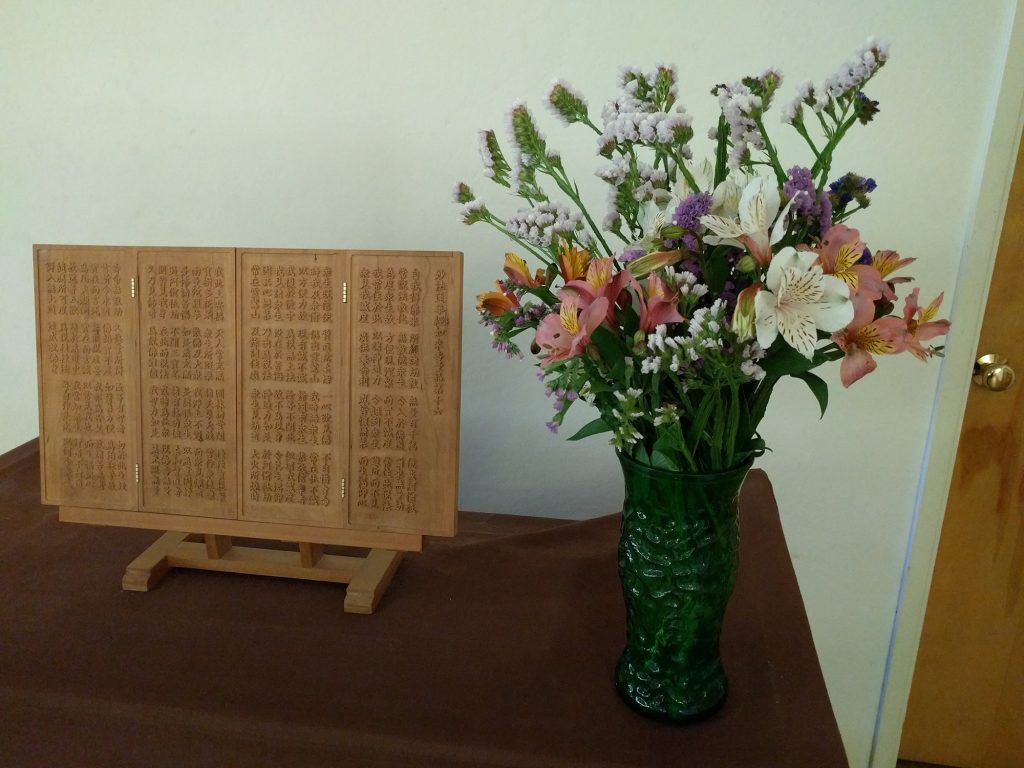 Flowers next to hand-carved wooden tablet of Chapter 16 of the Lotus Sutra.