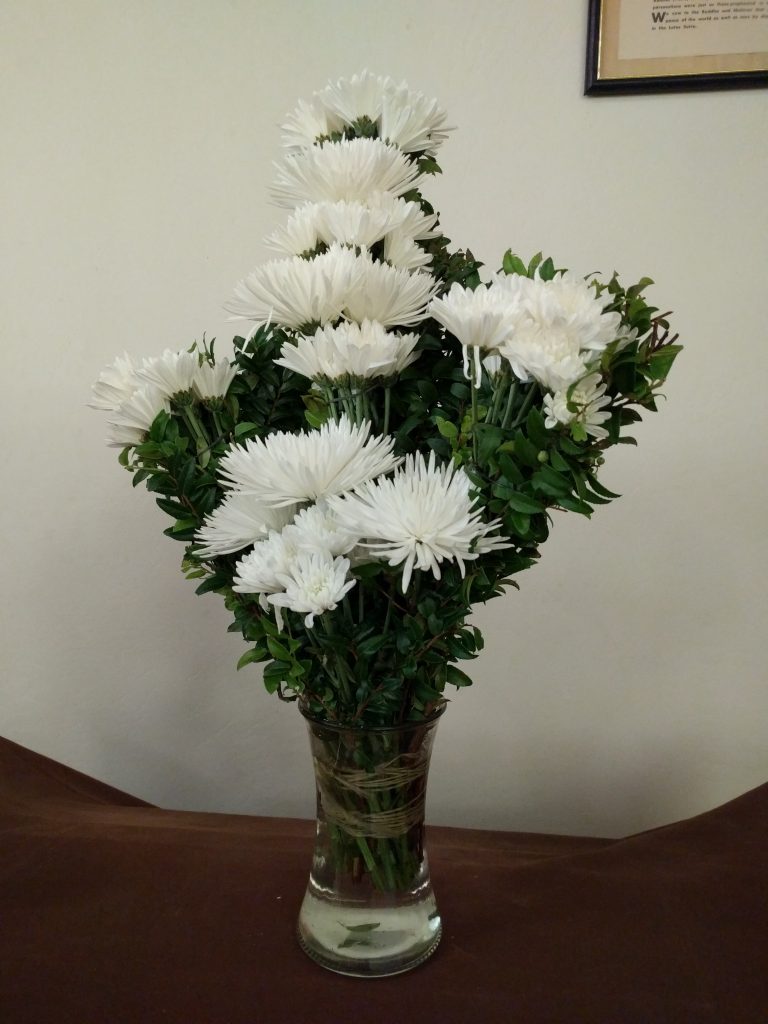 An arrangement of  white flowers in front of the church to the right of the altar.